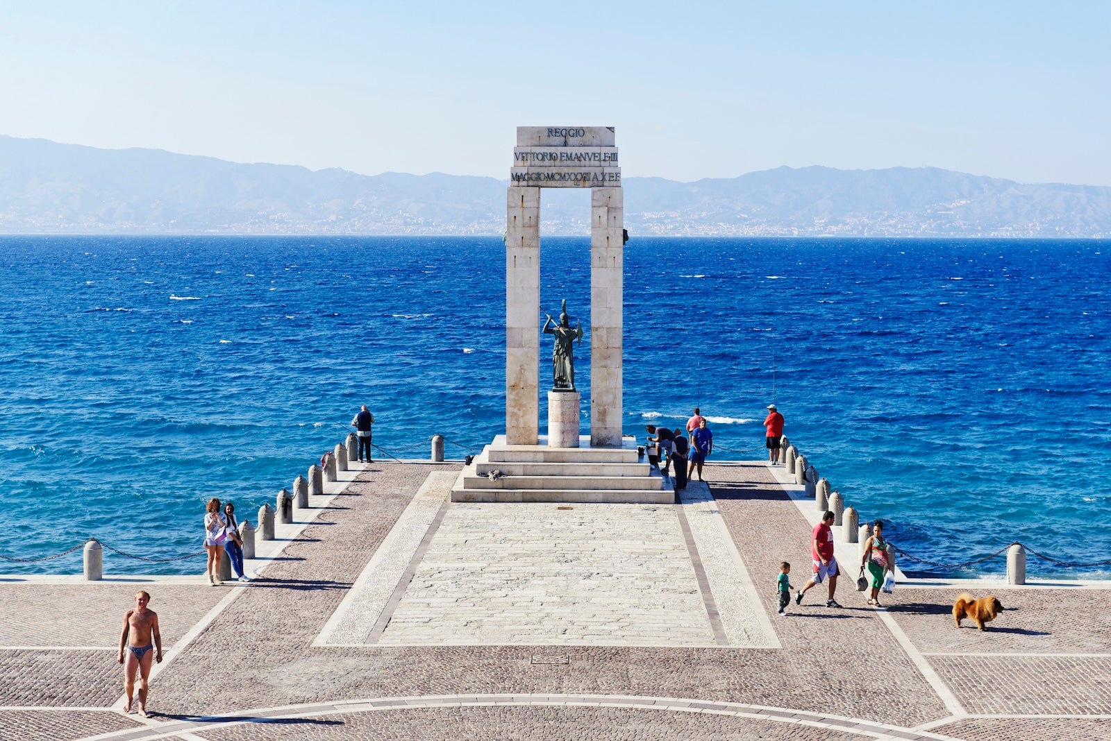 Here's why you should go to Calabria instead of Rome or Milan Reggio di Calabria, Calabria,Italy - September 27, 2013: Monument dedicated to Vittorio Emanuele III on the lungomare in Reggio di Calabria. The Strait of Messina and the coastline of Sicily in the background. People are walking near the monument or taking pictures.