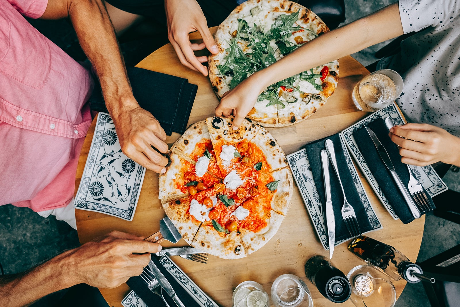 Family sharing pizza at a casual dining table. Hands of friends members reaching for pizza slices at a casual lunch setting