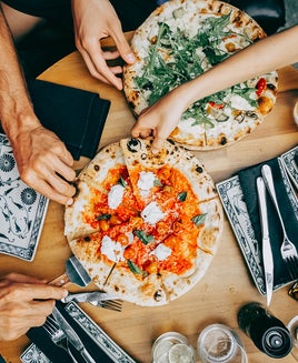 Family sharing pizza at a casual dining table. Hands of friends members reaching for pizza slices at a casual lunch setting