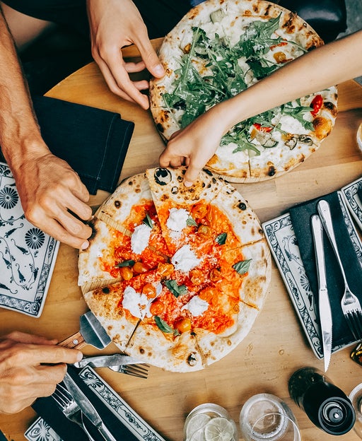 Family sharing pizza at a casual dining table. Hands of friends members reaching for pizza slices at a casual lunch setting