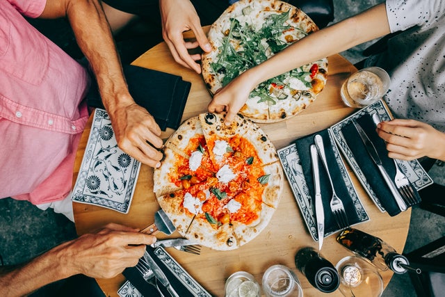 Family sharing pizza at a casual dining table. Hands of friends members reaching for pizza slices at a casual lunch setting