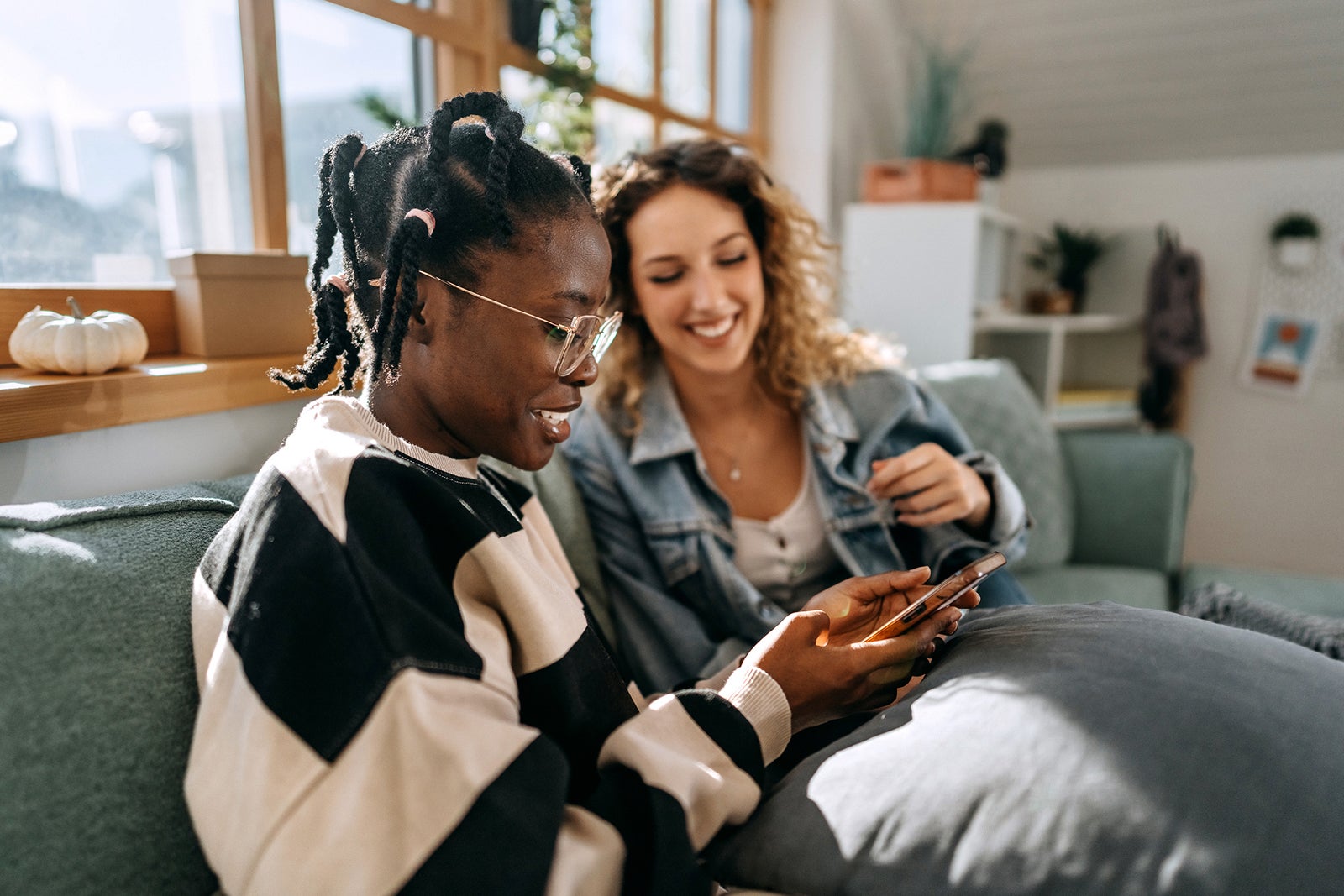 two women sitting on couch looking at phone