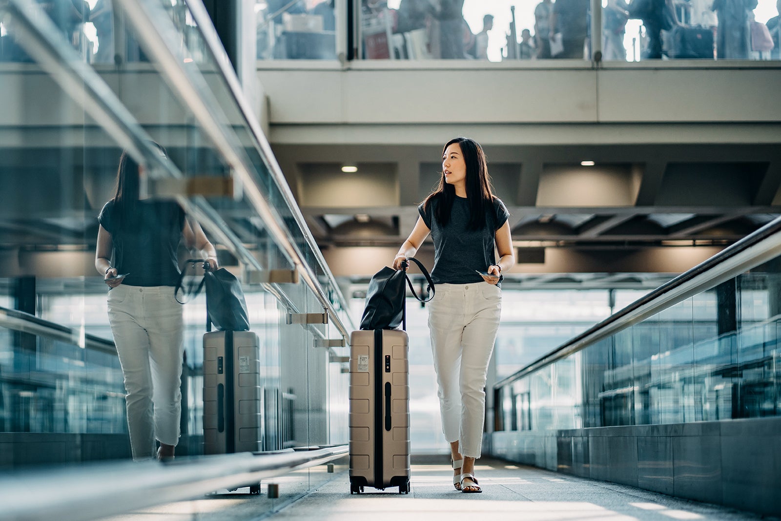 Young Asian woman with passport carrying suitcase walking in the airport concourse
