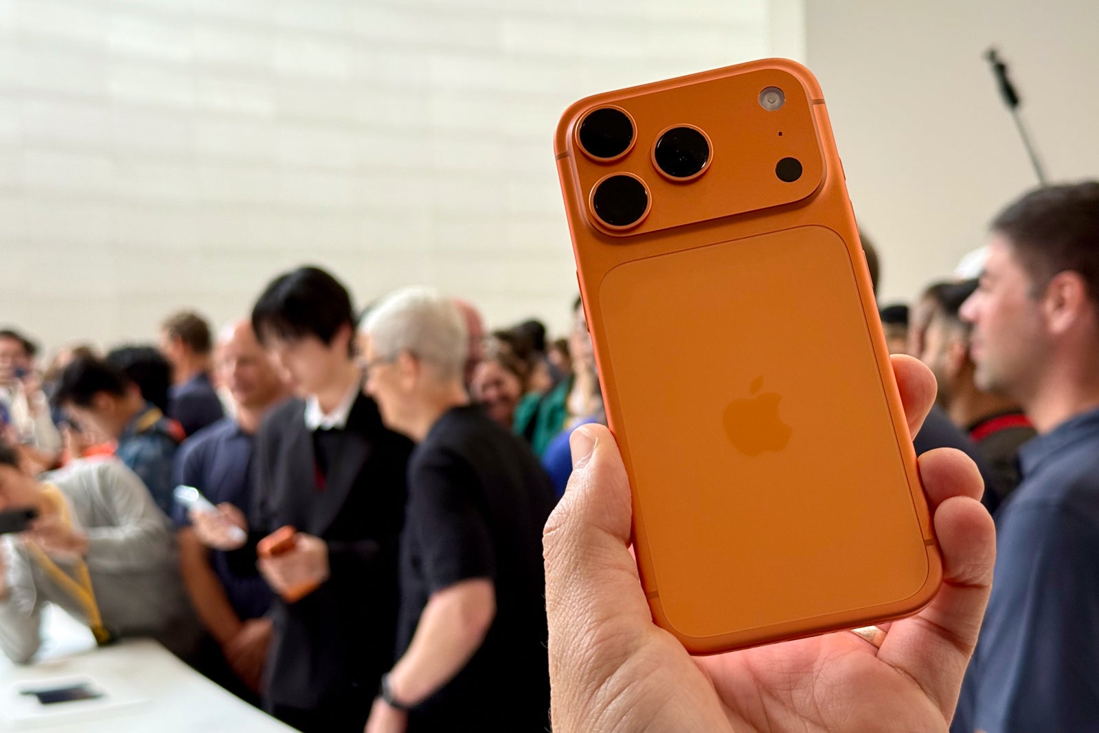 a hand holding an orange iPhone in front of a crowd