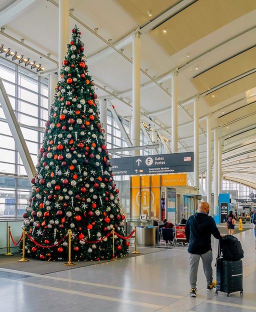 person walking luggage through airport near a decorated christmas tree