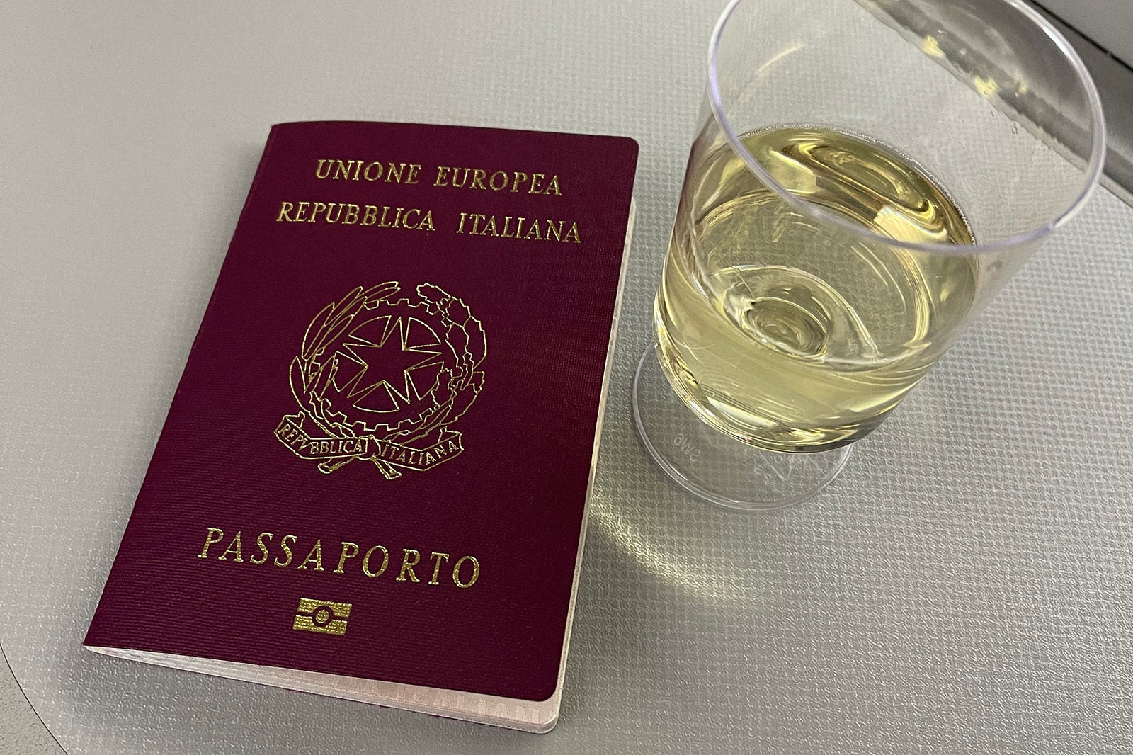 An Italian passport and glass of white wine on a business class flight from Charlotte to Frankfurt