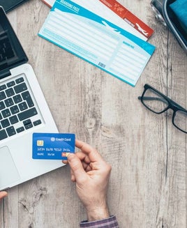 Someone holding a credit card while using laptop and packing for trip