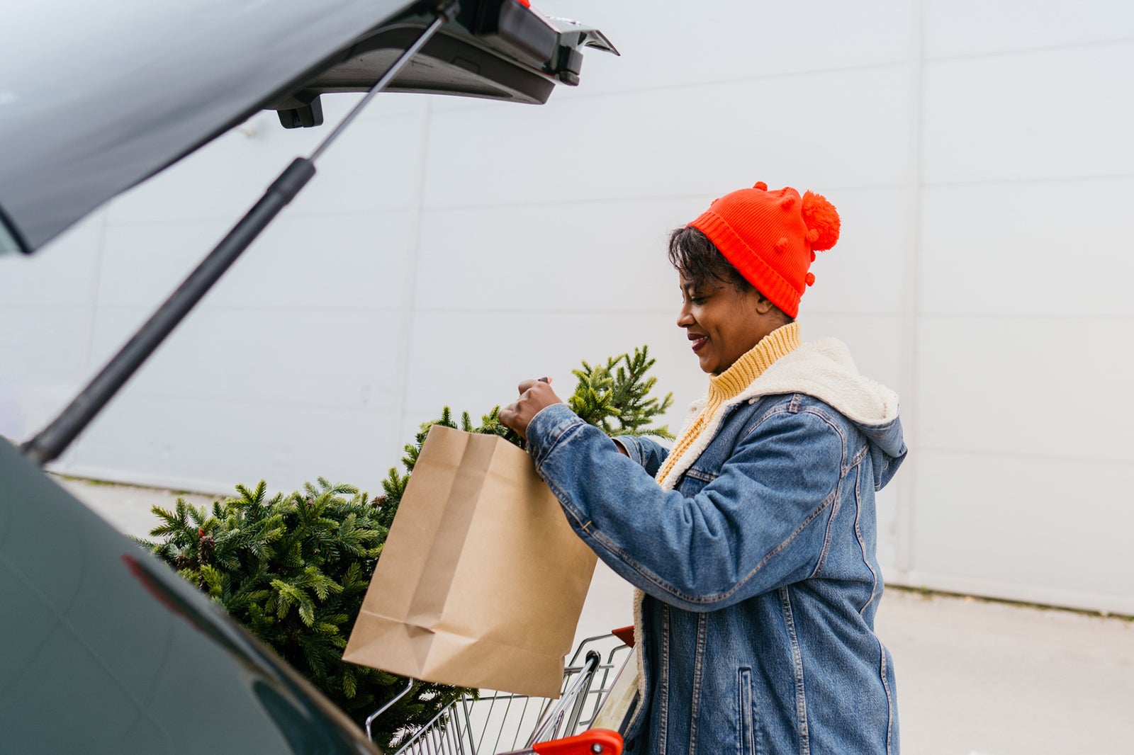 Photo of a young woman packing a Christmas tree in the trunk of her car, after buying it at a local market; getting ready for the upcoming holiday season.