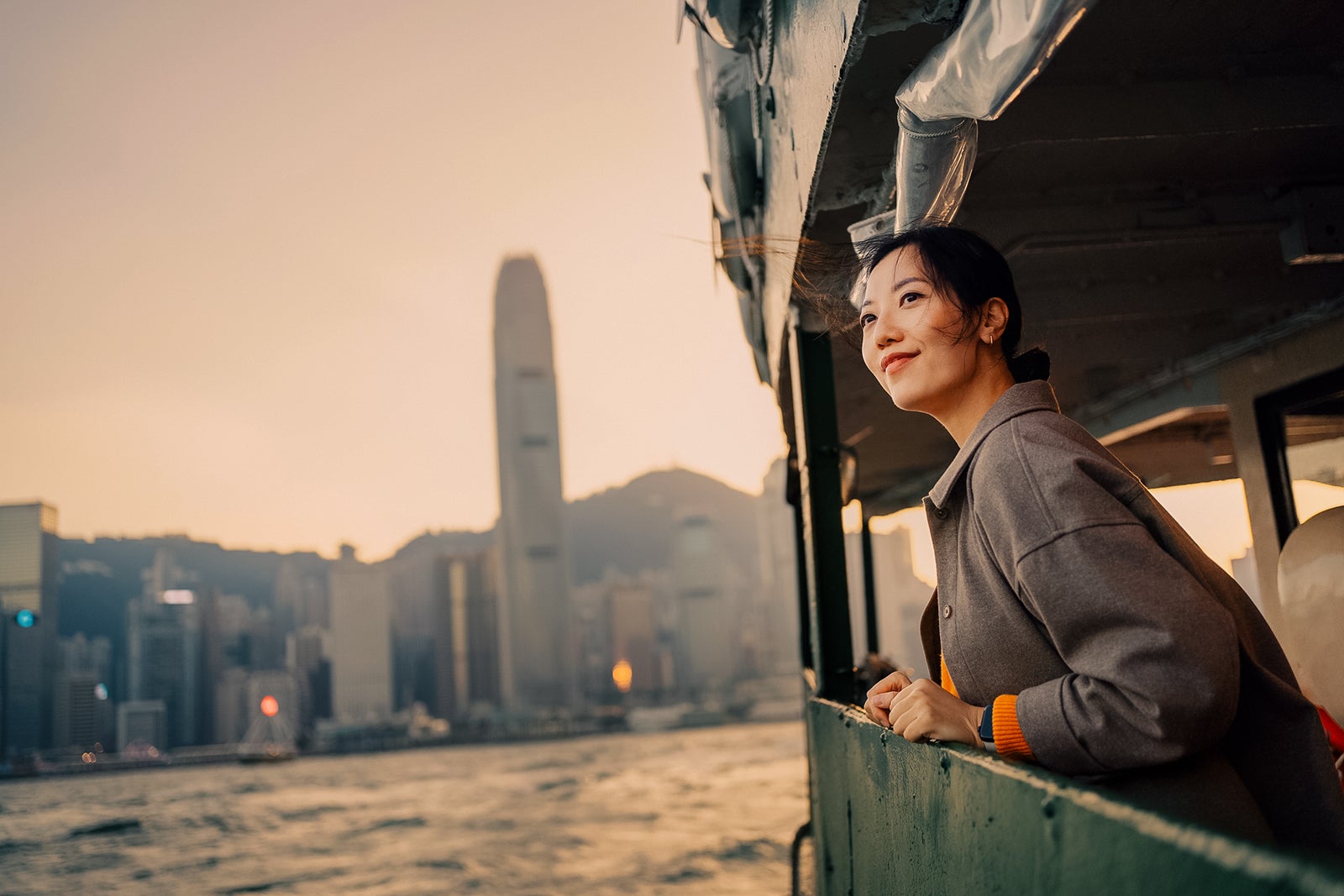 female traveller enjoying the spectacular iconic city skyline of Hong Kong and Victoria harbour while riding on the Star Ferry at dusk. Exploring local cultures in the city.
