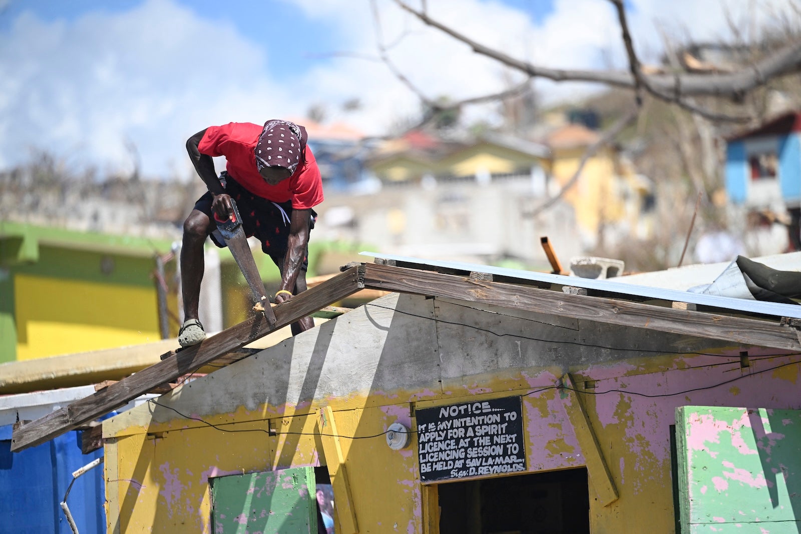 A man saws a piece of wood to repair the roof of a shop in Westmoreland, Jamaica, following the passage of Hurricane Melissa, on November 2, 2025. Planes and helicopters carrying humanitarian aid headed to Jamaica on October 31, three days after Melissa slammed into the island nation and killed at least 19 people. Information Minister Dana Morris Dixon told a briefing that authorities had "quite credible" reports of possibly five additional deaths but had not yet been able to confirm.