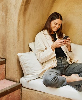 Wide shot woman sitting in alcove using phone at boutique hotel