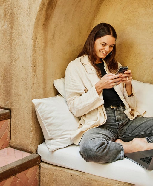 Wide shot woman sitting in alcove using phone at boutique hotel