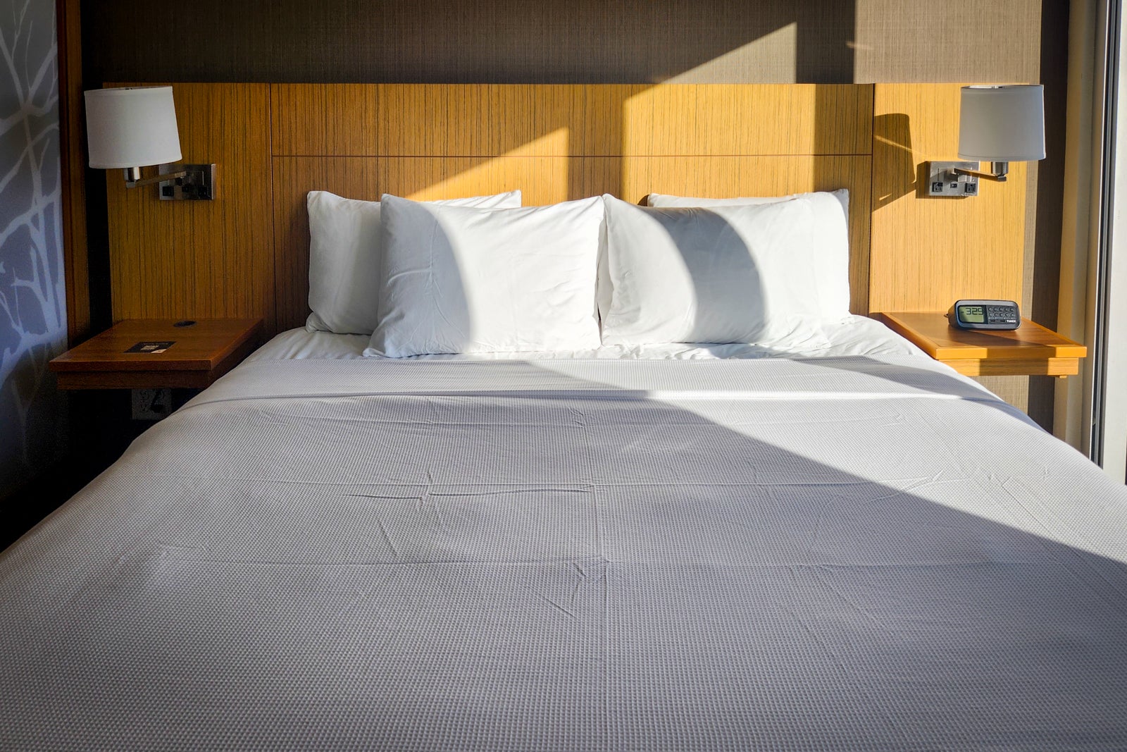 hotel bed with wooden headboard and sunlight streaming through window