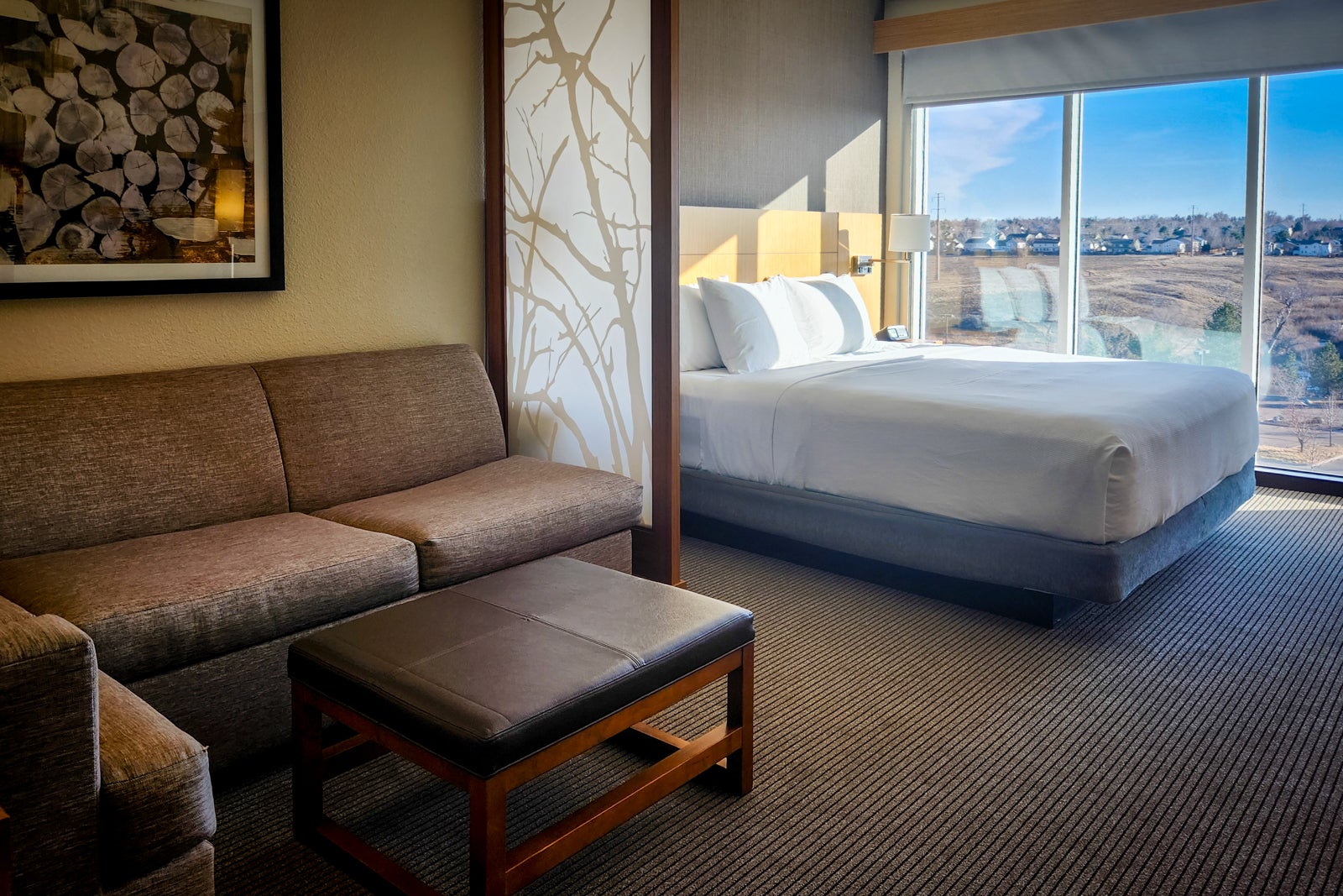 hotel room with bed, couch, and windows overlooking hills