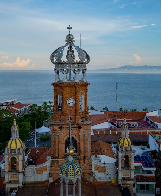 Drone aerial view of the iconic Puerto Vallarta Cathedral in Jalisco, Mexico, featuring its distinctive crown tower and colonial architecture overlooking the Pacific Ocean.