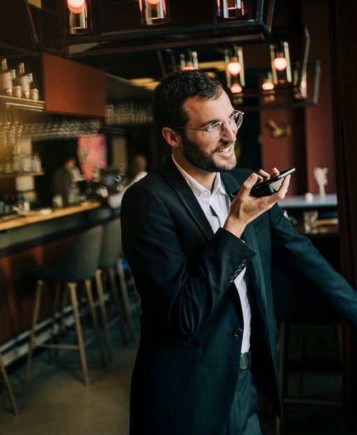 Smiling businessman sending voicemail through smart phone while standing in hotel lobby