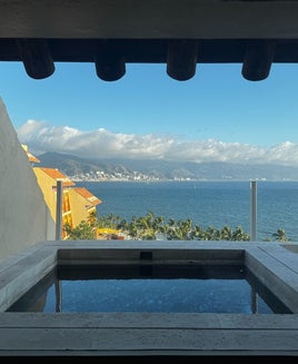 View of balcony plunge pool overlooking blue water and mountains with palm trees