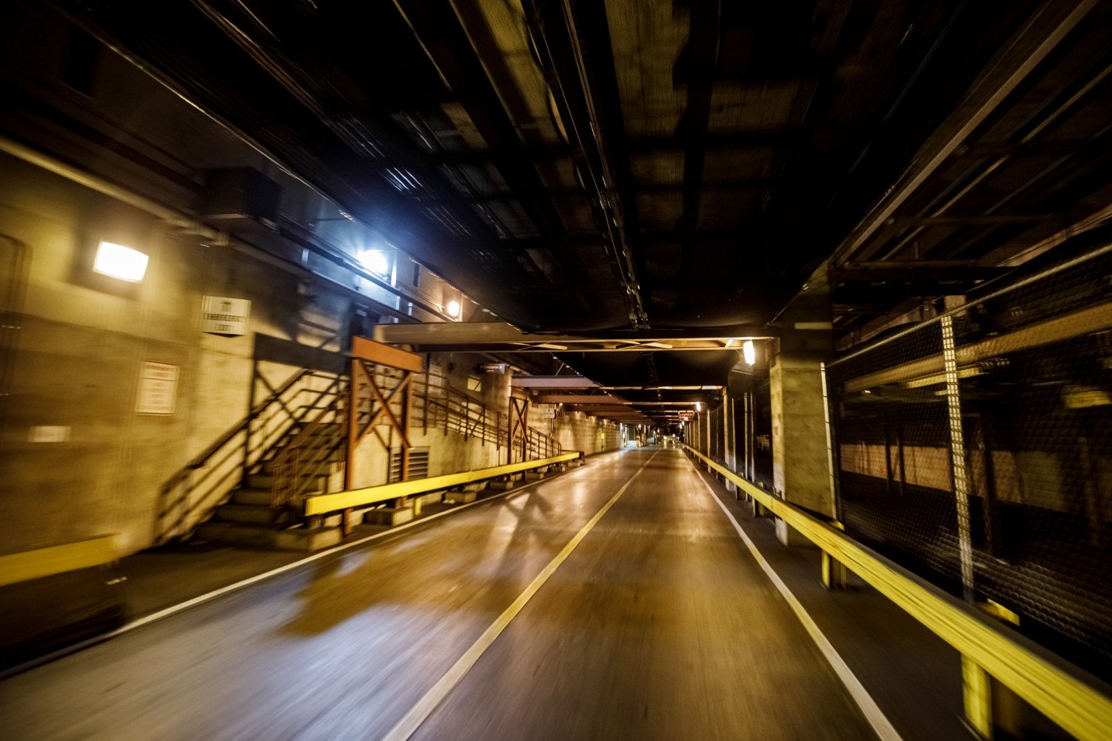 Empty underground tunnel with yellow guardrails, illuminated lights, and a curved road fading into the distance.