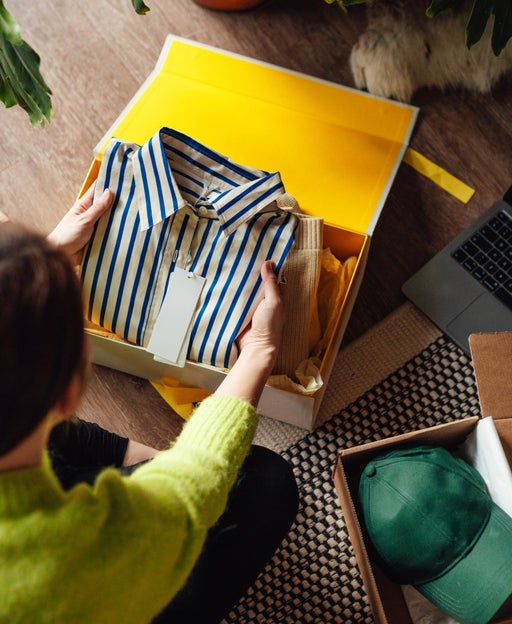 Elevated view of young woman unboxing a delivery from home shopping, with a laptop by her side.